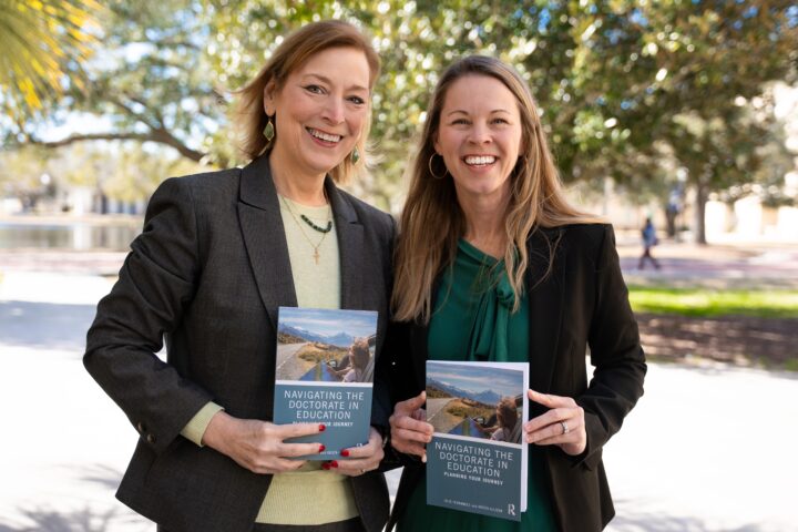 Two women holding the same book that is called navigating the doctorate in education.