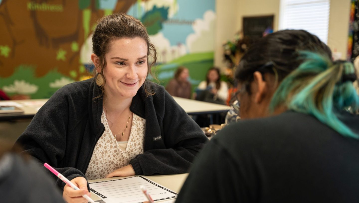 Two women with a pen and paper and talking to each other