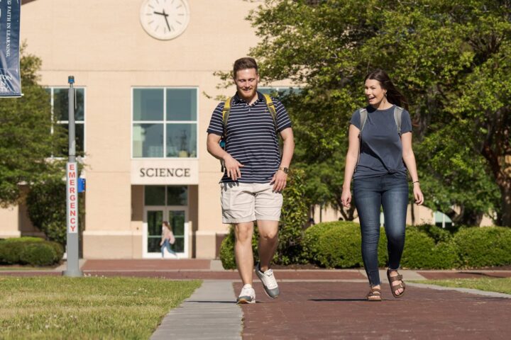 Two students walking down a brick path on CSU's campus with the science building in the background.