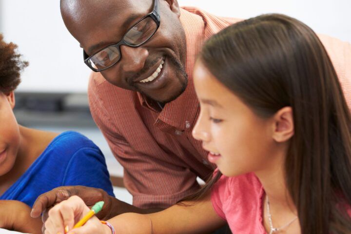 Teacher helping an elementary student who is writing in her notebook.