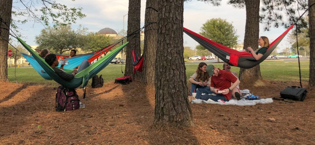 Students hanging in their Eno hammocks in a wooded section of campus.