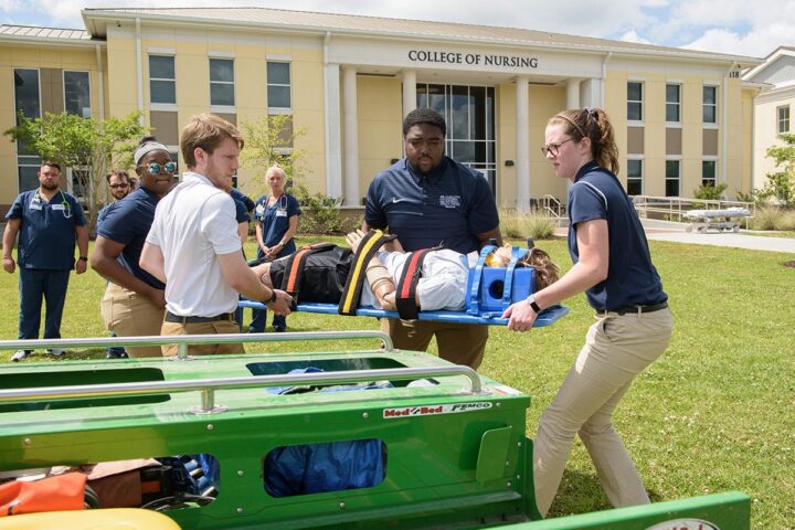 Athletic Trainers carry a simulation mannequin on a board at the College of Nursing.