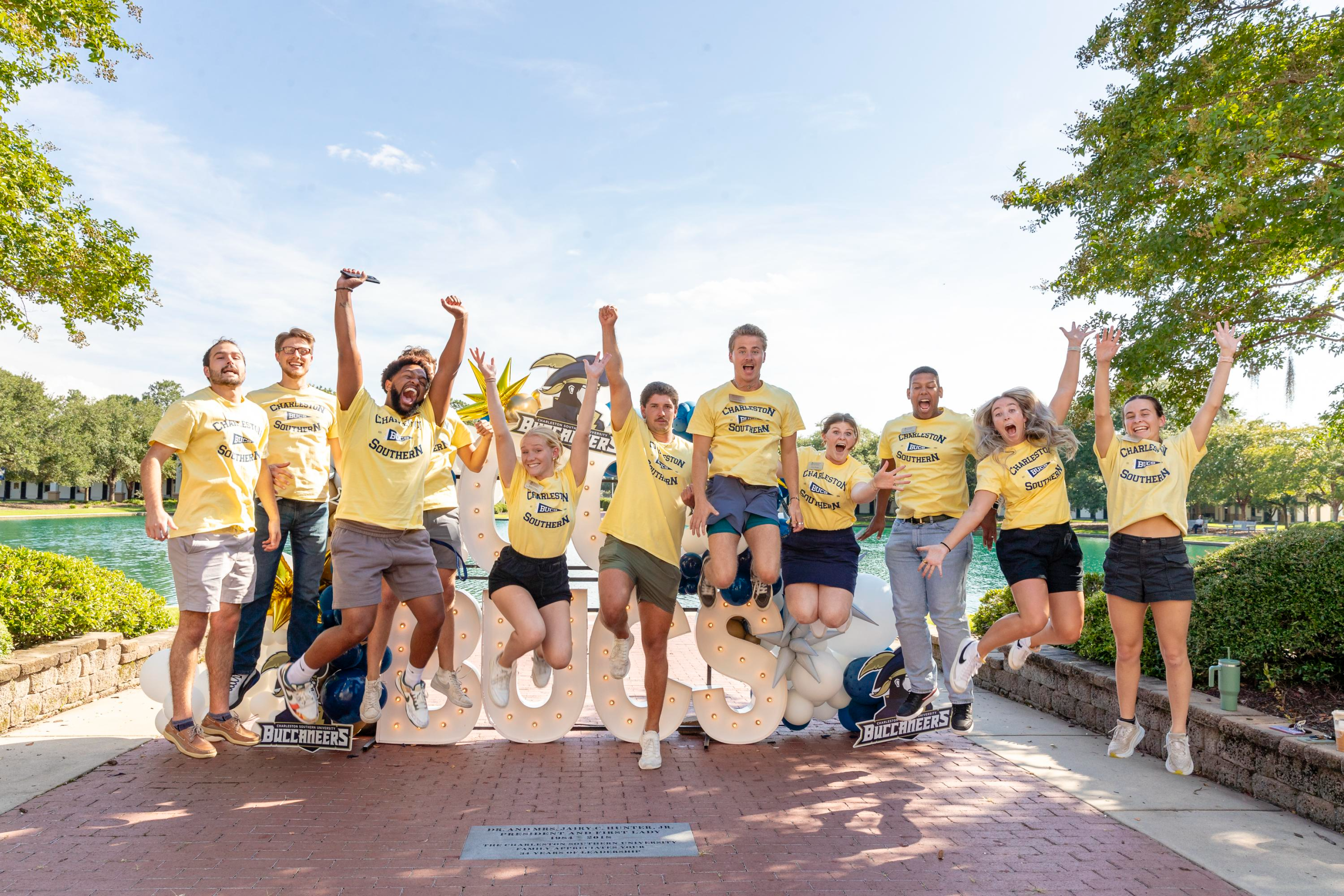 Group of CSU students wearing yellow t-shirts jump in front of the campus pond