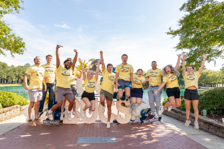 Group of CSU students wearing yellow t-shirts jump in front of the campus pond