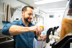 A man working in the hustleduck truck pouring a drink in a cup for a customer