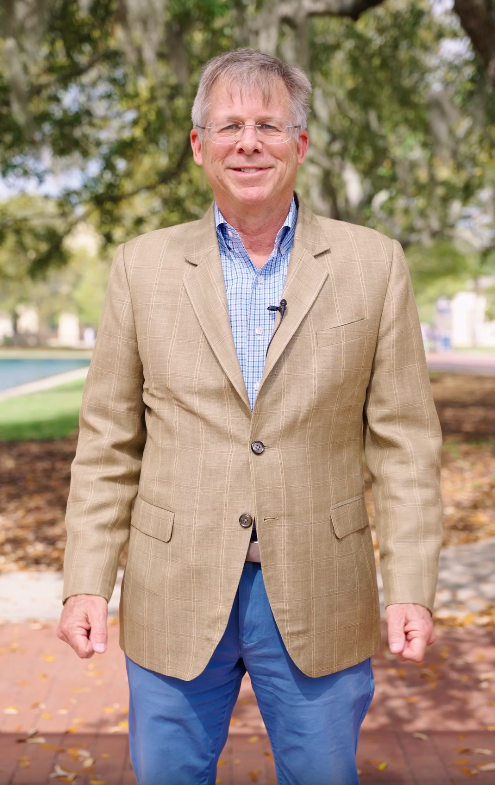 Male CSU professor in sport coat and blue jeans stands on brick walkway talking to the camera