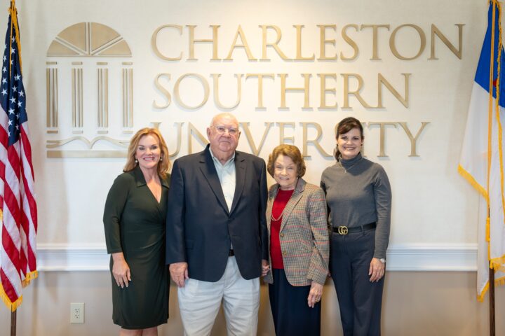 Four people taking a picture between two flags and CSU in the background